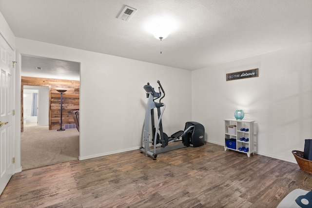 workout area featuring visible vents, wooden walls, baseboards, and wood finished floors