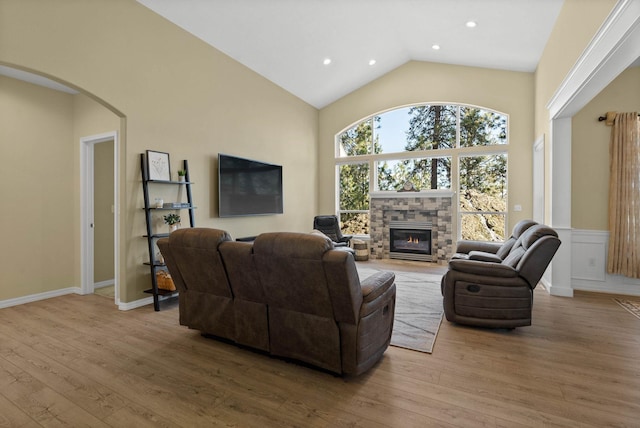 living area with arched walkways, wood finished floors, a fireplace, high vaulted ceiling, and recessed lighting