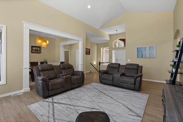 living area with high vaulted ceiling, baseboards, visible vents, and wood finished floors