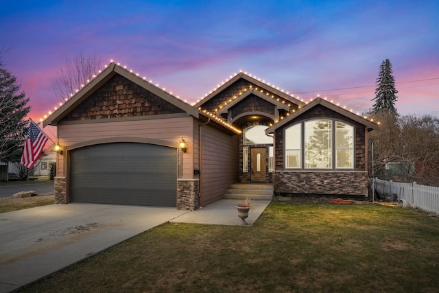 view of front facade featuring concrete driveway, a lawn, an attached garage, fence, and stone siding