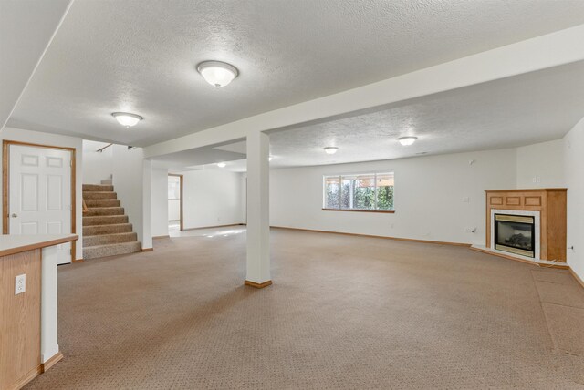 below grade area featuring light carpet, baseboards, stairway, and a glass covered fireplace