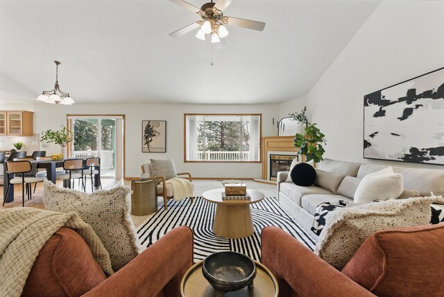 living room with a glass covered fireplace, baseboards, and ceiling fan with notable chandelier