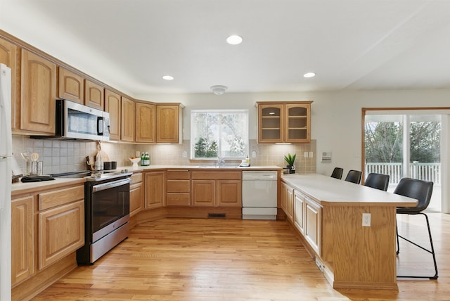 kitchen with stainless steel appliances, a breakfast bar, a peninsula, a sink, and light wood-style floors