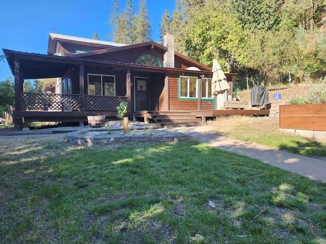 view of front facade featuring a deck, a front yard, metal roof, and a chimney