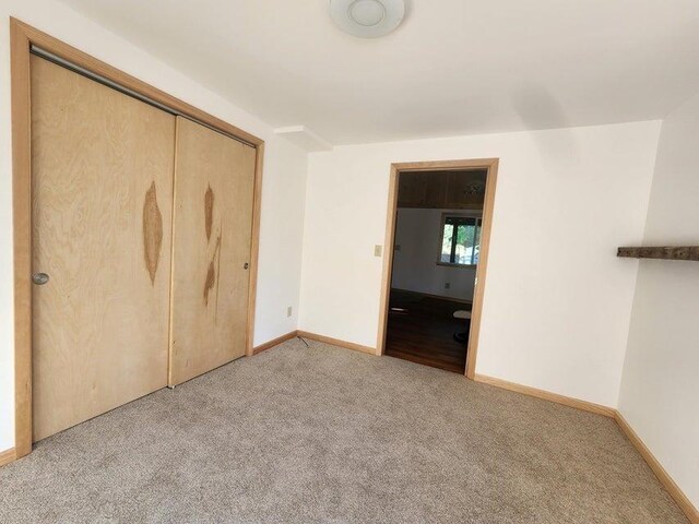 unfurnished bedroom featuring baseboards, a closet, and light colored carpet