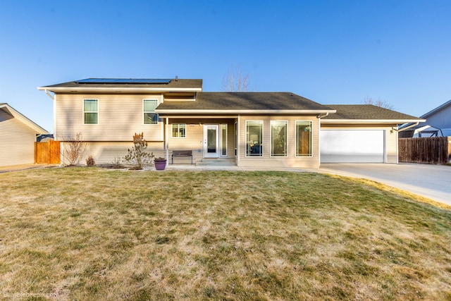 view of front facade featuring concrete driveway, fence, solar panels, and a front yard