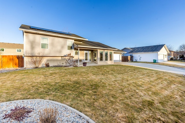 rear view of property with a lawn, fence, solar panels, and concrete driveway