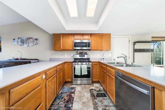 kitchen featuring appliances with stainless steel finishes, a tray ceiling, a sink, and a peninsula