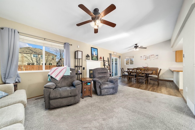 carpeted living room featuring lofted ceiling, wood finished floors, visible vents, baseboards, and a glass covered fireplace