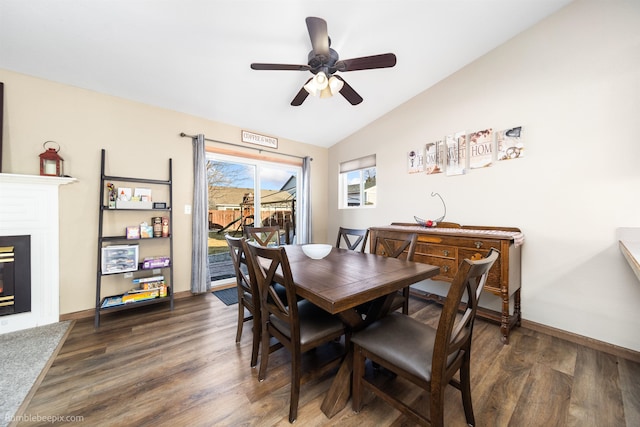 dining room featuring lofted ceiling, ceiling fan, dark wood-style flooring, baseboards, and a glass covered fireplace