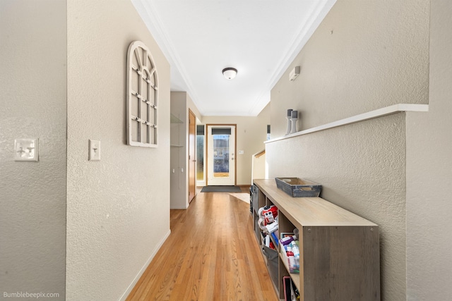 hall featuring a textured wall, ornamental molding, and light wood-style flooring