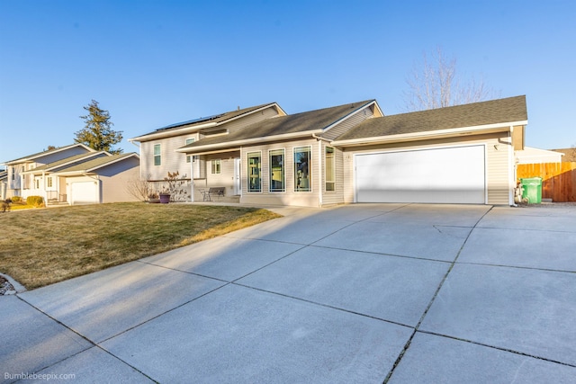 view of front of house featuring a front yard, roof mounted solar panels, fence, a garage, and driveway