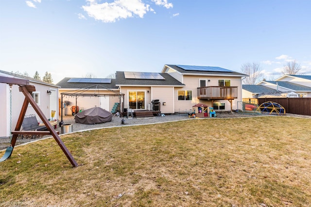 back of property with a lawn, fence, a gazebo, roof mounted solar panels, and a playground