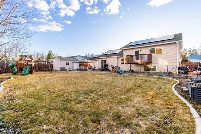 back of property featuring a yard, a playground, a fenced backyard, and roof mounted solar panels