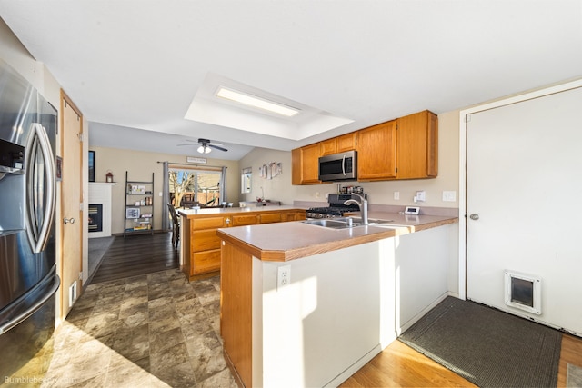 kitchen featuring brown cabinets, stainless steel appliances, a glass covered fireplace, a sink, and a peninsula