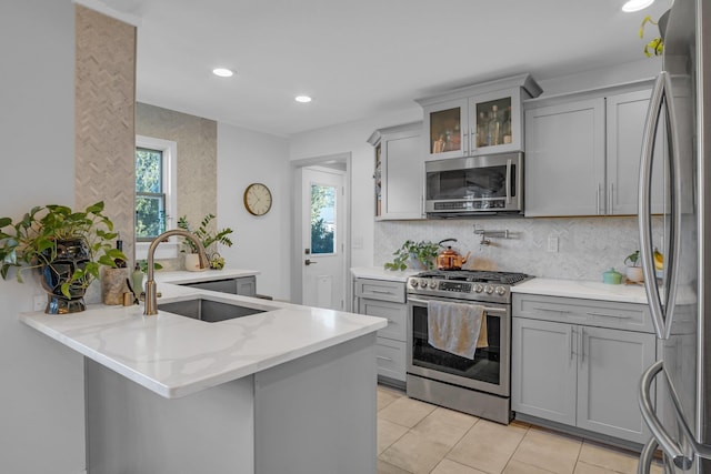 kitchen featuring stainless steel appliances, a peninsula, a sink, and gray cabinetry