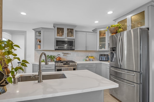 kitchen with decorative backsplash, light stone counters, appliances with stainless steel finishes, gray cabinetry, and a sink