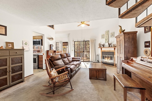 living room featuring ceiling fan, a tile fireplace, a textured ceiling, and light colored carpet