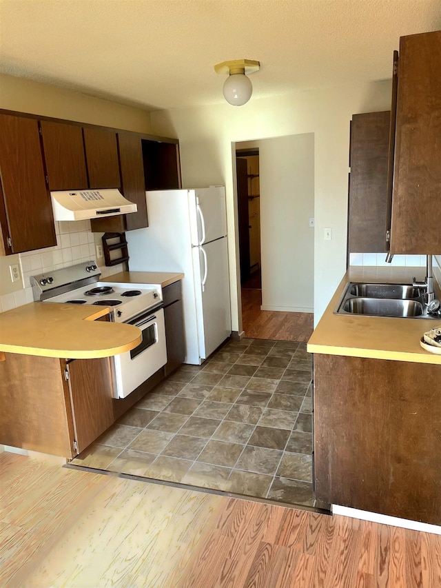 kitchen featuring under cabinet range hood, white appliances, wood finished floors, a sink, and decorative backsplash