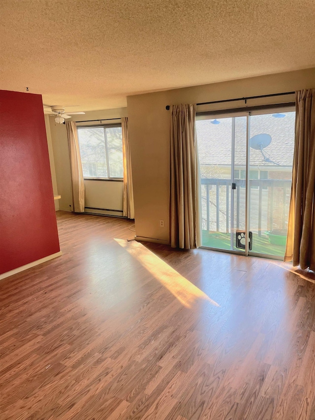 interior space featuring a textured ceiling, baseboard heating, wood finished floors, and baseboards