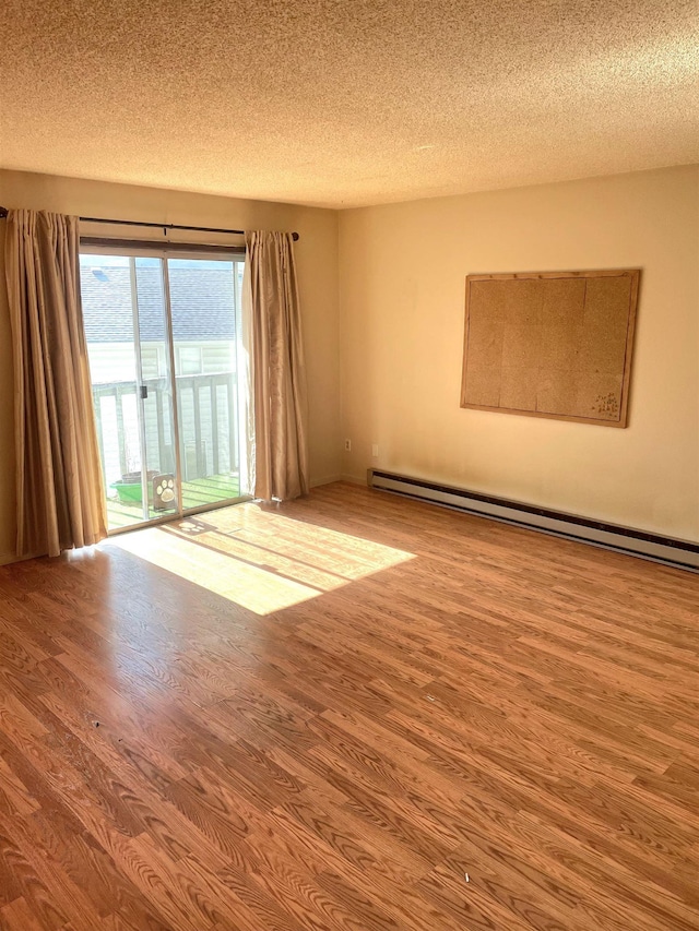 empty room featuring a textured ceiling, a baseboard heating unit, and wood finished floors