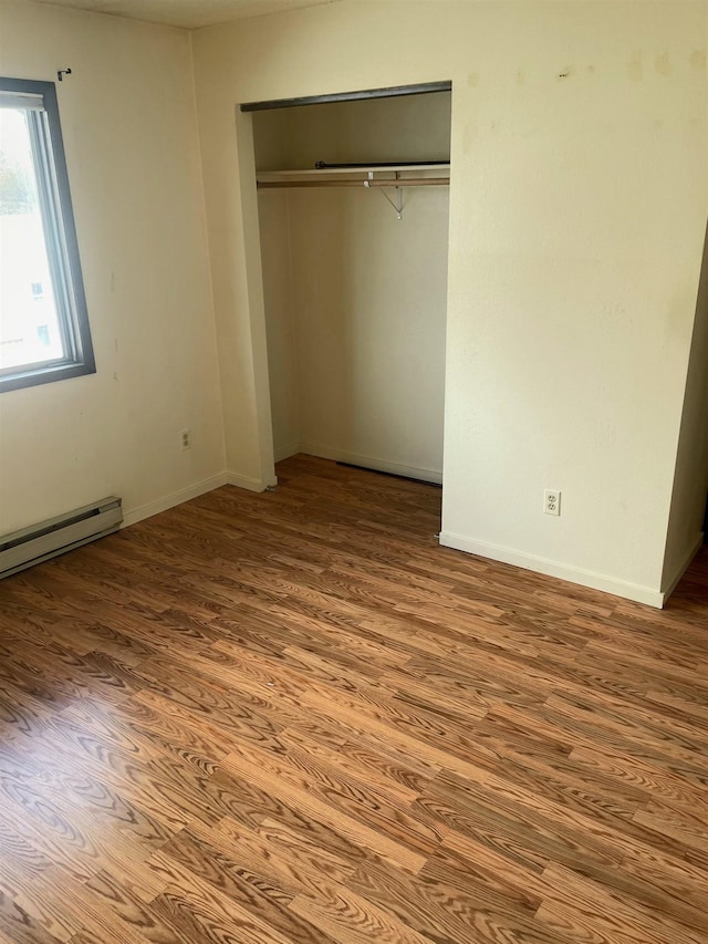 unfurnished bedroom featuring a closet, baseboards, baseboard heating, and wood finished floors