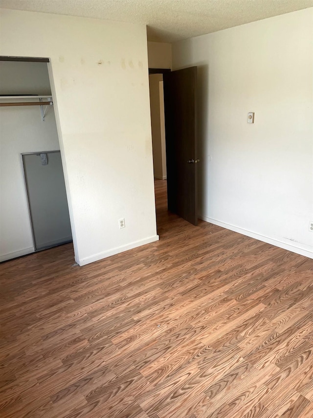 unfurnished bedroom featuring a textured ceiling, baseboards, and wood finished floors