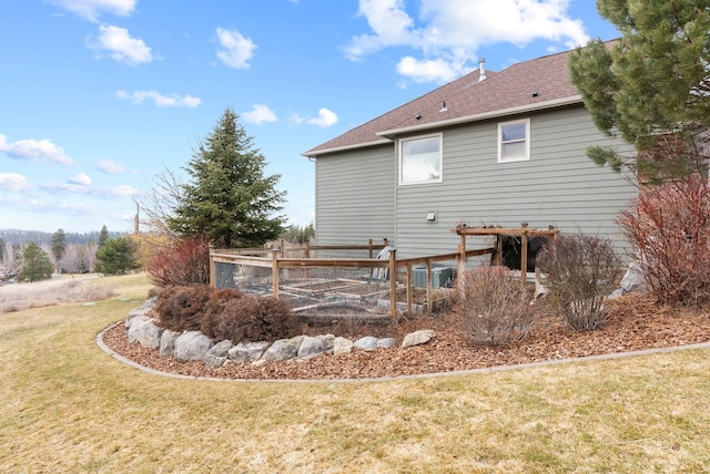 rear view of property with a shingled roof, a lawn, and fence