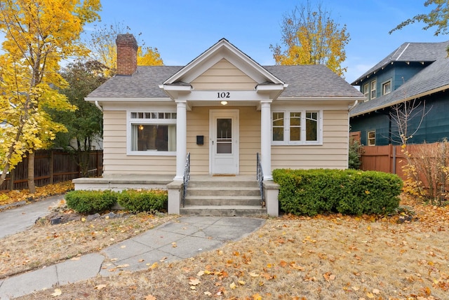 bungalow-style home with a shingled roof, a chimney, and fence