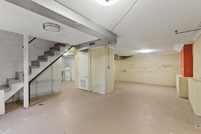 finished basement with stairs, visible vents, and electric water heater