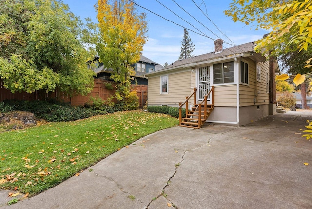 view of front facade featuring entry steps, a chimney, fence, and a front yard