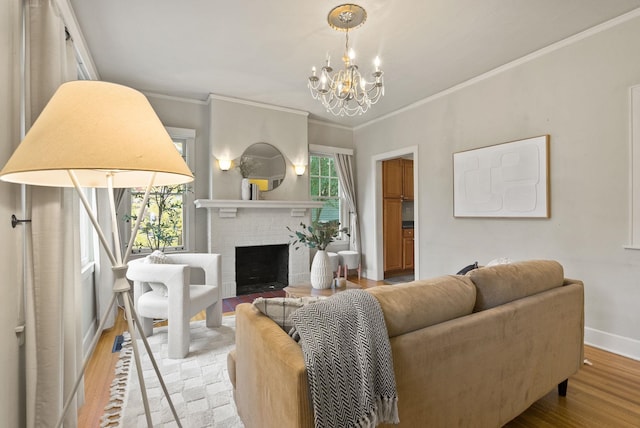 living room with baseboards, an inviting chandelier, crown molding, light wood-type flooring, and a brick fireplace