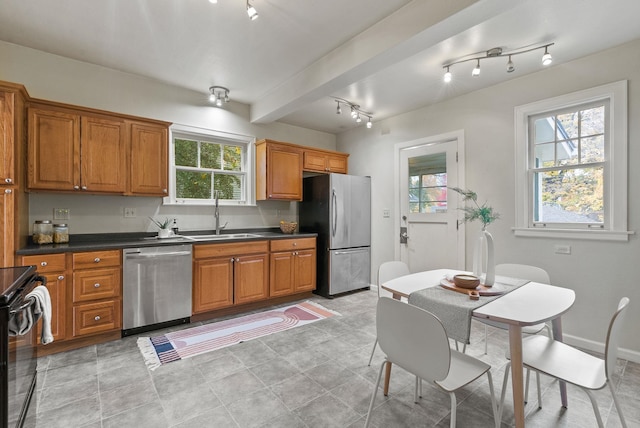 kitchen featuring stainless steel appliances, dark countertops, brown cabinetry, and a sink