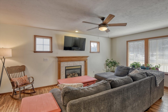 living area featuring ceiling fan, a textured ceiling, wood finished floors, a tile fireplace, and baseboards