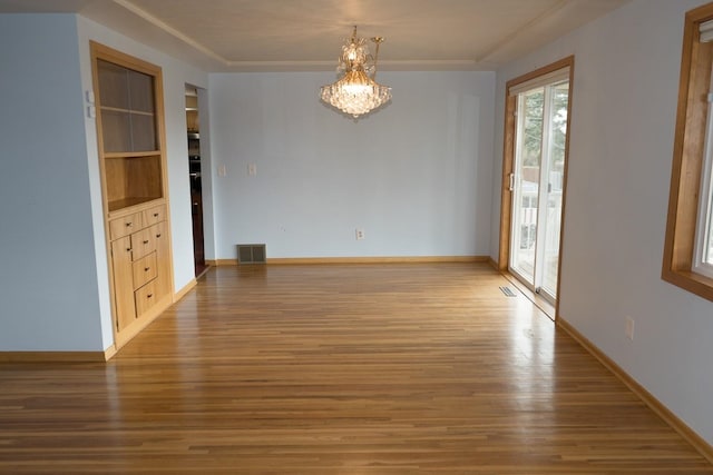 unfurnished dining area featuring baseboards, wood finished floors, visible vents, and an inviting chandelier