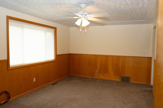 unfurnished room with a wainscoted wall, wooden walls, and visible vents