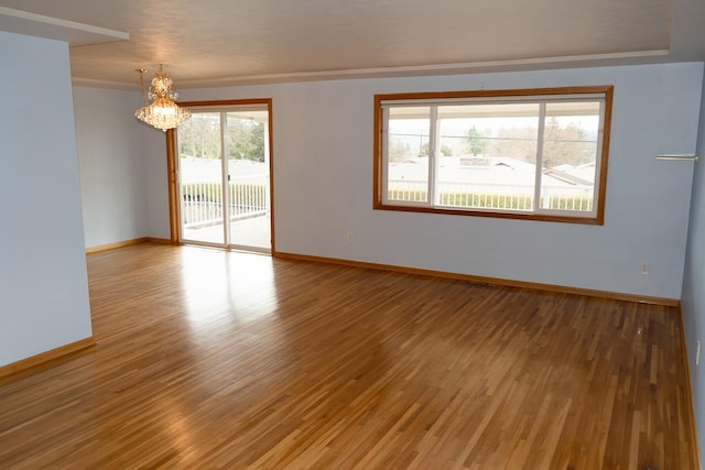 spare room with a chandelier, light wood-style flooring, and baseboards