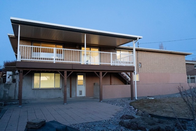 back of house featuring a patio area, stairs, brick siding, and stucco siding