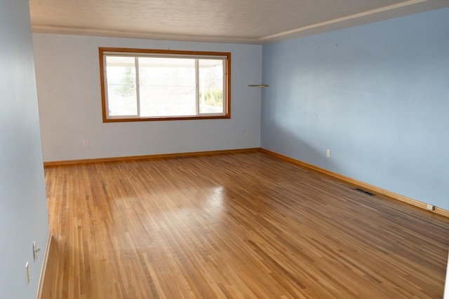 empty room featuring light wood-type flooring, baseboards, and visible vents