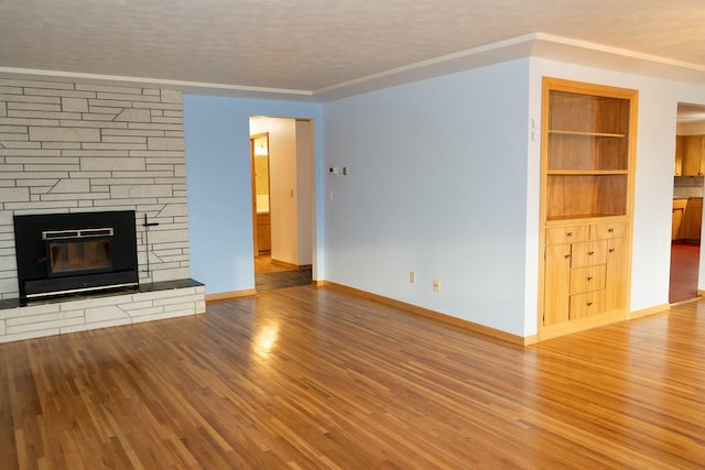 unfurnished living room with ornamental molding, a stone fireplace, baseboards, and wood finished floors