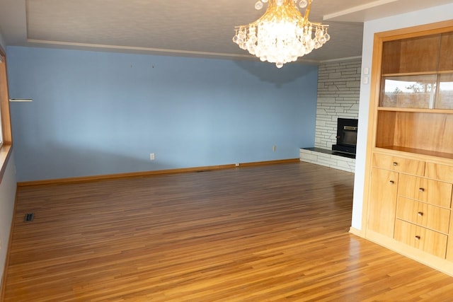 unfurnished living room with a stone fireplace, wood finished floors, baseboards, ornamental molding, and an inviting chandelier