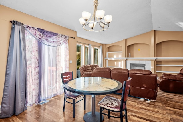 dining area with lofted ceiling, a tiled fireplace, wood finished floors, and a notable chandelier