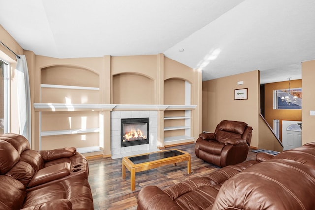 living area with a tiled fireplace, lofted ceiling, wood finished floors, built in shelves, and a chandelier