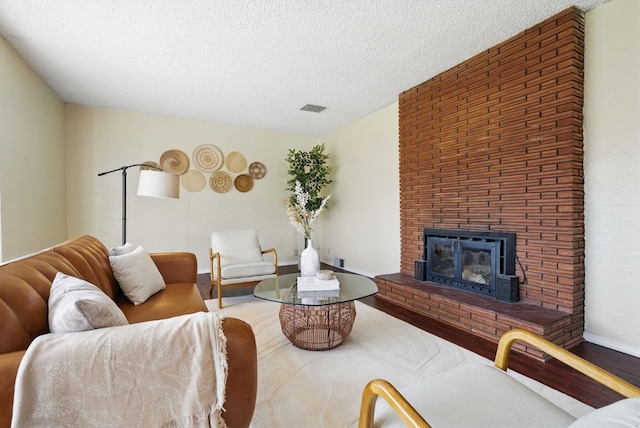 living area with visible vents, a brick fireplace, a textured ceiling, wood finished floors, and baseboards