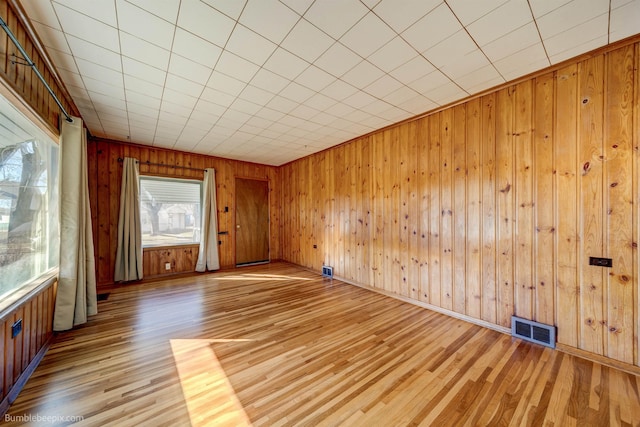 spare room with light wood-type flooring, visible vents, and wood walls