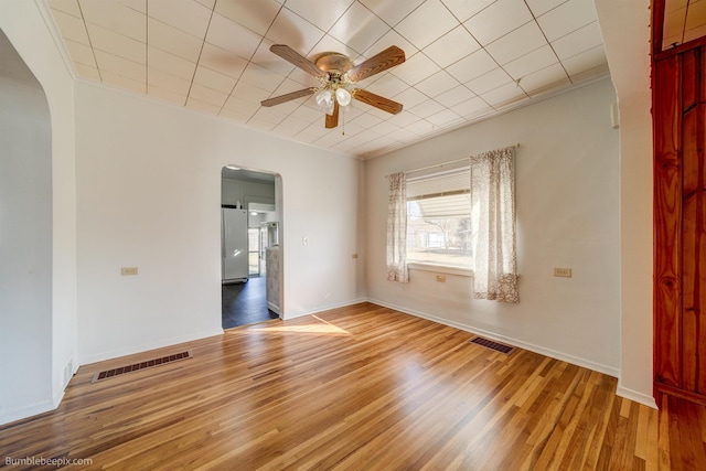 unfurnished room with arched walkways, visible vents, ceiling fan, and wood finished floors