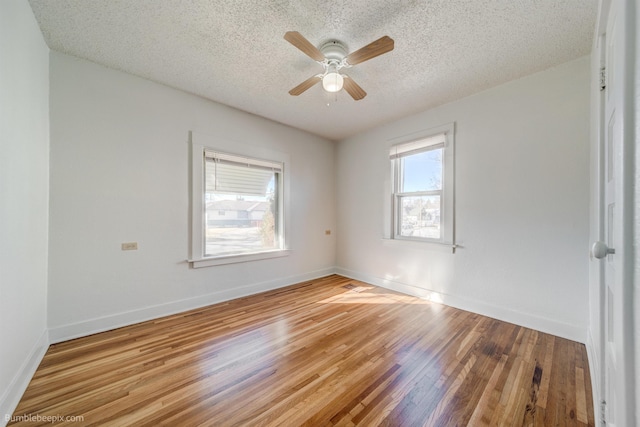 spare room featuring a textured ceiling, baseboards, wood finished floors, and a ceiling fan