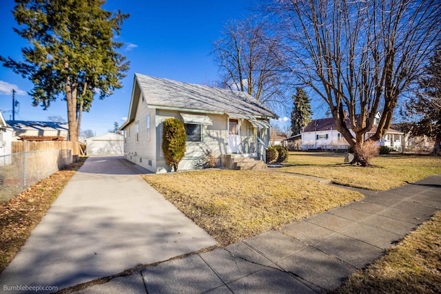 bungalow with fence, a front lawn, and an outbuilding