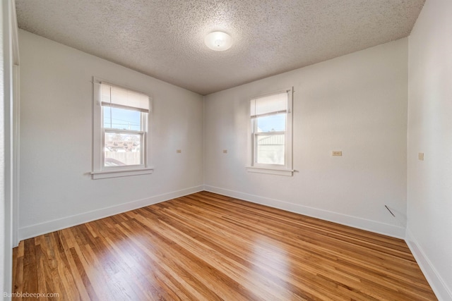 unfurnished room with a textured ceiling, light wood finished floors, plenty of natural light, and baseboards