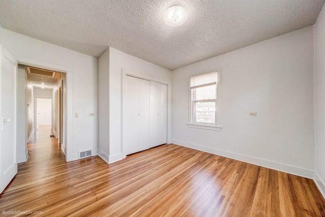 unfurnished bedroom with a closet, visible vents, a textured ceiling, light wood-type flooring, and baseboards